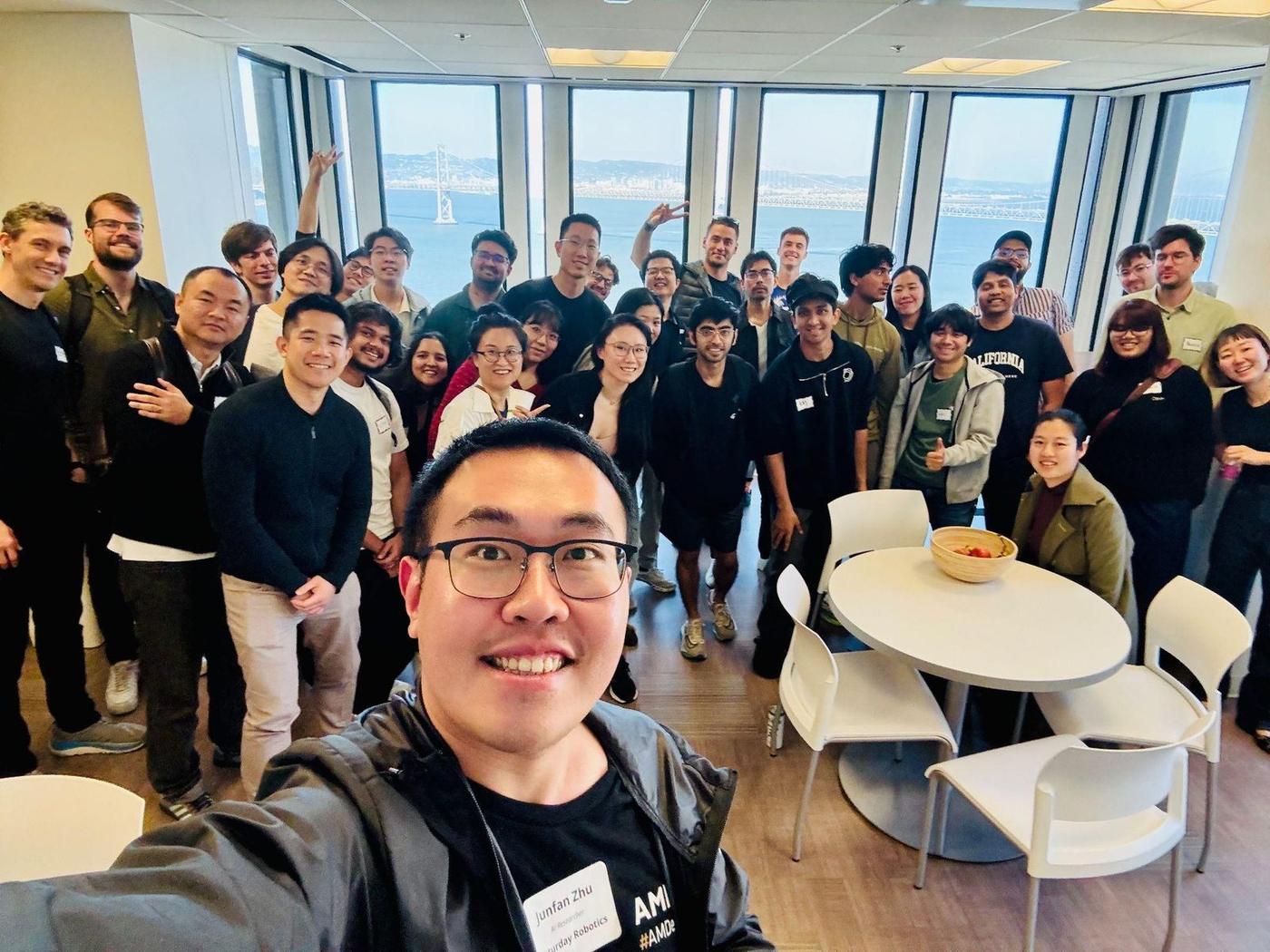 Junfan Zhu takes a selfie with dozens of participants at a Saturday Robotics session in San Francisco, with the Bay Bridge behind them